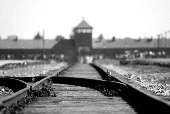 black and white camera pointing from the ground in the middle of railroad tracks looking toward the main train building at auschwitz birkemnau concentration camp where the trains arrived with people - tours to Auschwitz from Warsaw