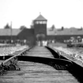 black and white camera pointing from the ground in the middle of railroad tracks looking toward the main train building at auschwitz birkemnau concentration camp where the trains arrived with people - tours to Auschwitz from Warsaw