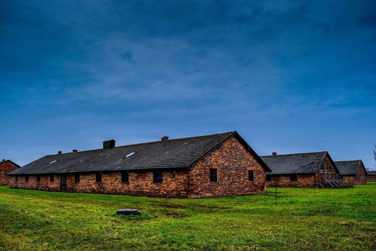 blue skies and green grass-one story red building with windows in Auschwitz Birkenau- tours-of-auschwitz-from-warsaw