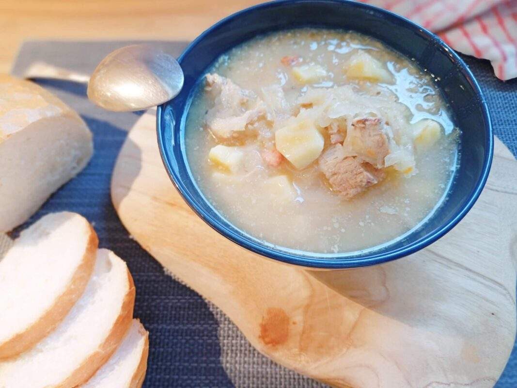 polish kapusniak in a bowl with kielbasa, a spoon on the left and sliced bread