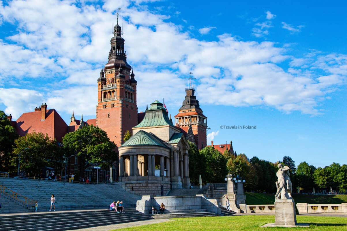 The iconic red-brick tower of the Ducal Castle in Szczecin stands proudly under a sky dotted with clouds, with the terraced Haken Terrace in the foreground. Marked with a 'Travels in Poland' watermark, this image showcases the historical and architectural splendor of Szczecin, one of the best cities in Poland.