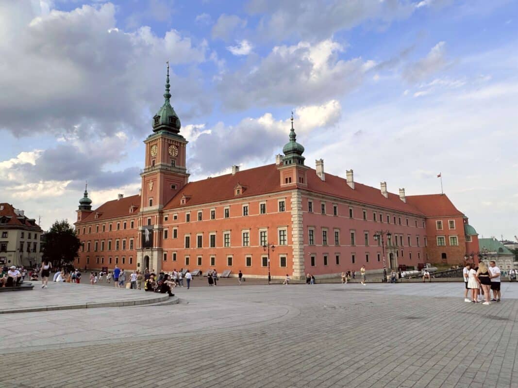 The Royal Castle in Warsaw, Poland, bathed in the soft glow of the evening sun, showcases historic architecture that's a highlight on Poland private tours, with visitors gathered in the spacious castle square.